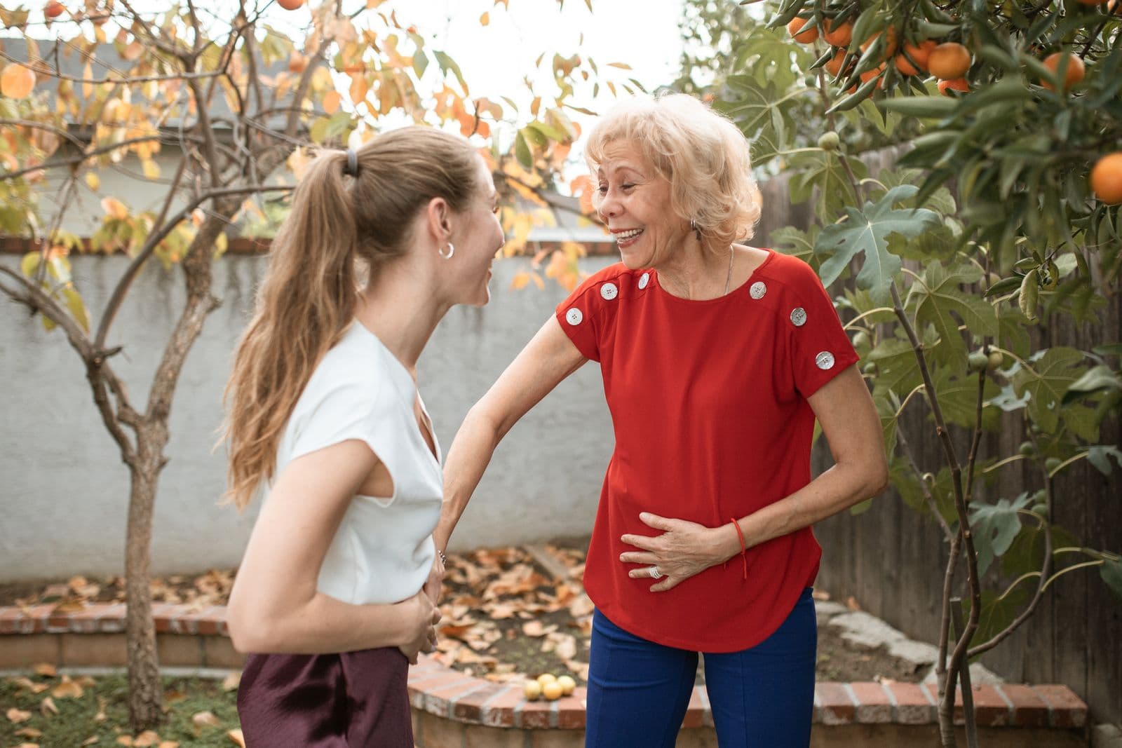 A care worker and an older person laughing together in a garden.